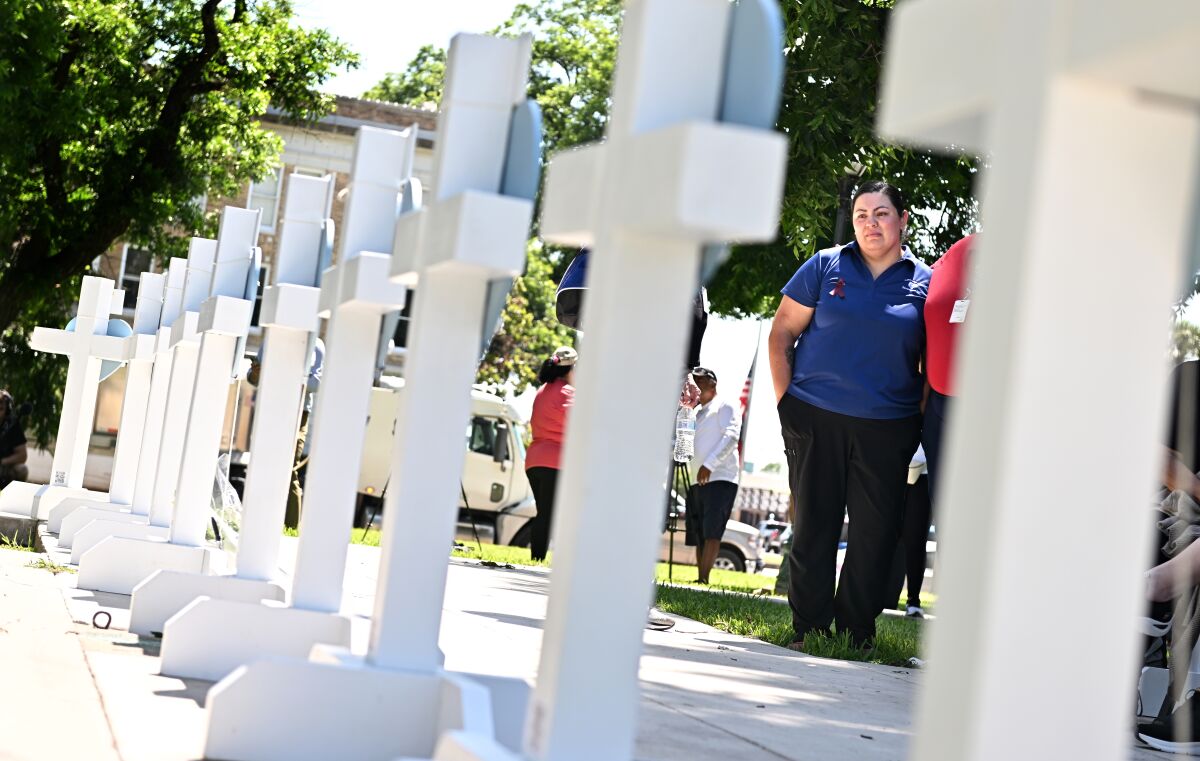People look at a row of white crosses set up on a sidewalk.
