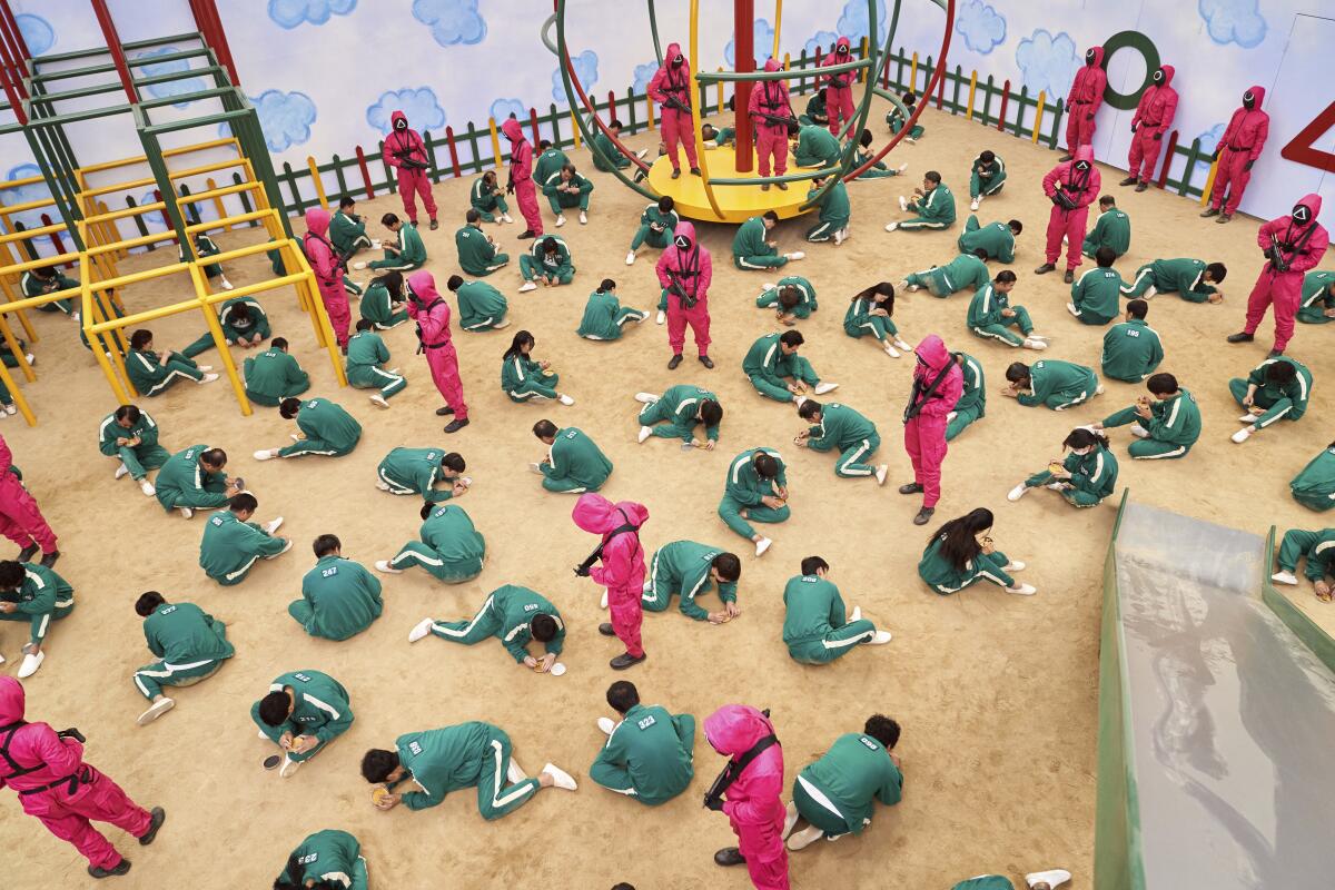 A number of people in green track suits crouched on the ground, guarded by people in pink track suits