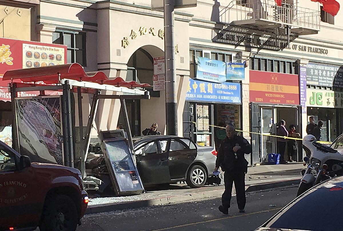 A police officer walks near the car that crashed into a bus shelter Friday afternoon in San Francisco's Chinatown.