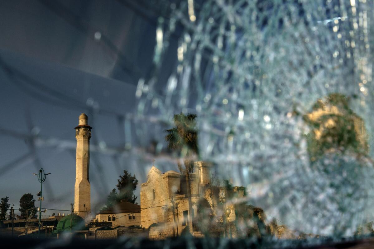 The minaret of the Al-Omari mosque and St. George Greek Orthodox church are reflected in the broken windshield of a vehicle sitting outside a synagogue in the mixed Arab-Jewish town of Lod, central Israel, Wednesday, May 26, 2021, in the wake of clashes between Arabs, police and Jews. The church shares a wall with a mosque and sits across from a synagogue in an area known as the triangle of religions. Like Jews and Arabs across the country, communities in Lod are on edge as the future of peaceful coexistence in mixed cities remains in question. (AP Photo/David Goldman)