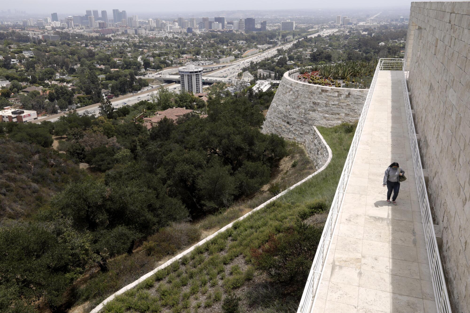 A visitor walks on a Getty Center sidewalk overlooking the 405 Freeway and Westside skyline