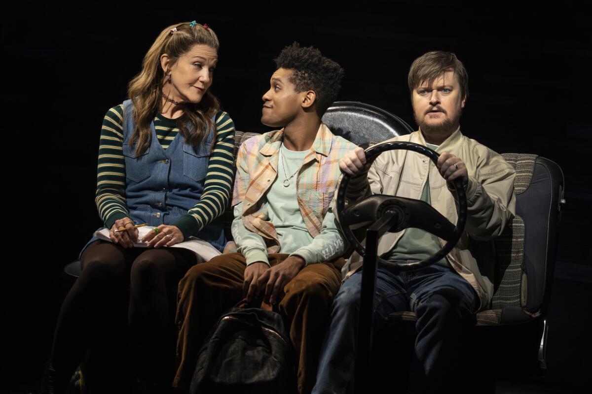 three people onstage in a pretend car 