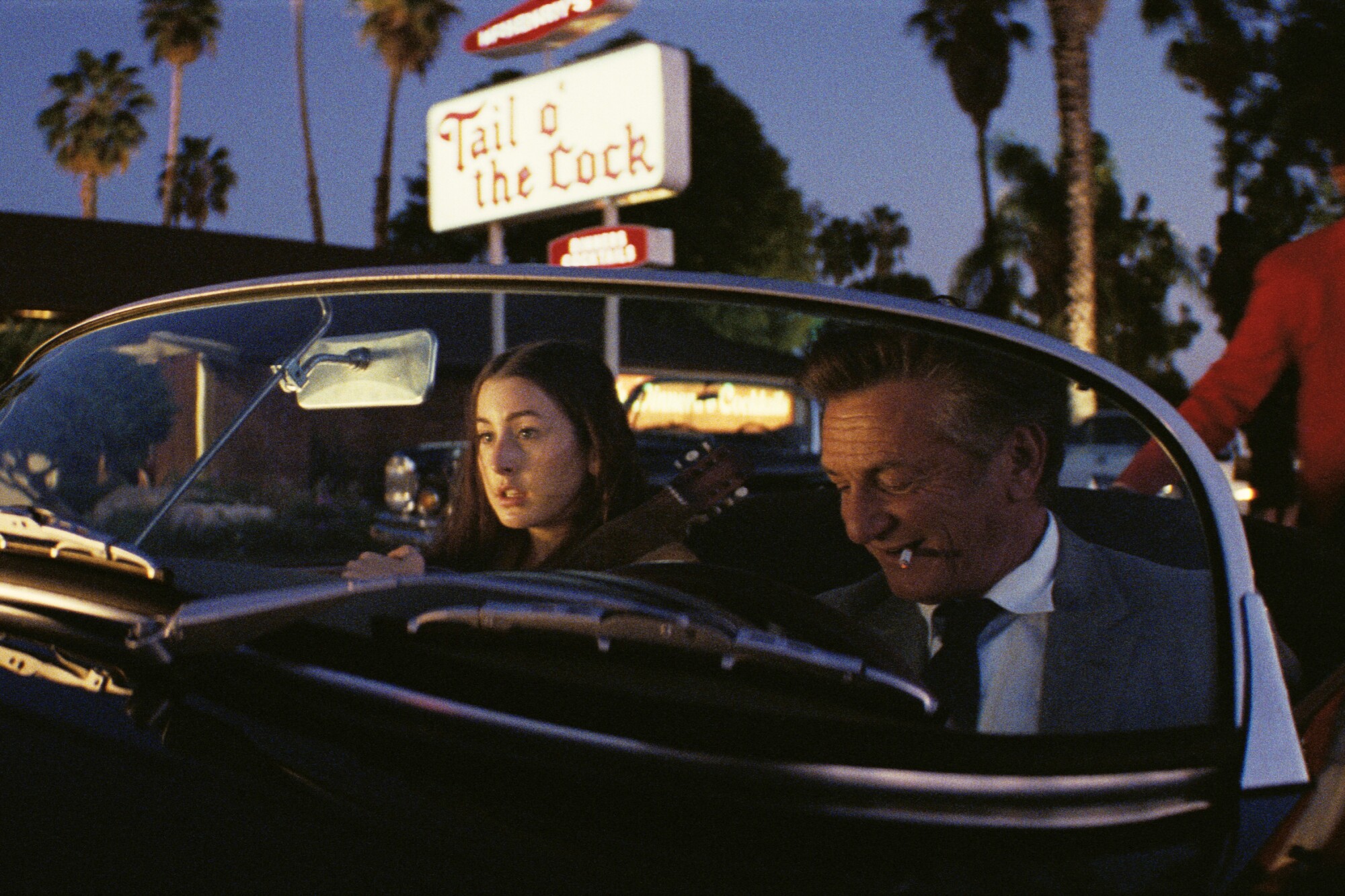 A young woman and older man sit in a vintage convertible outside a restaurant in "Licorice Pizza."