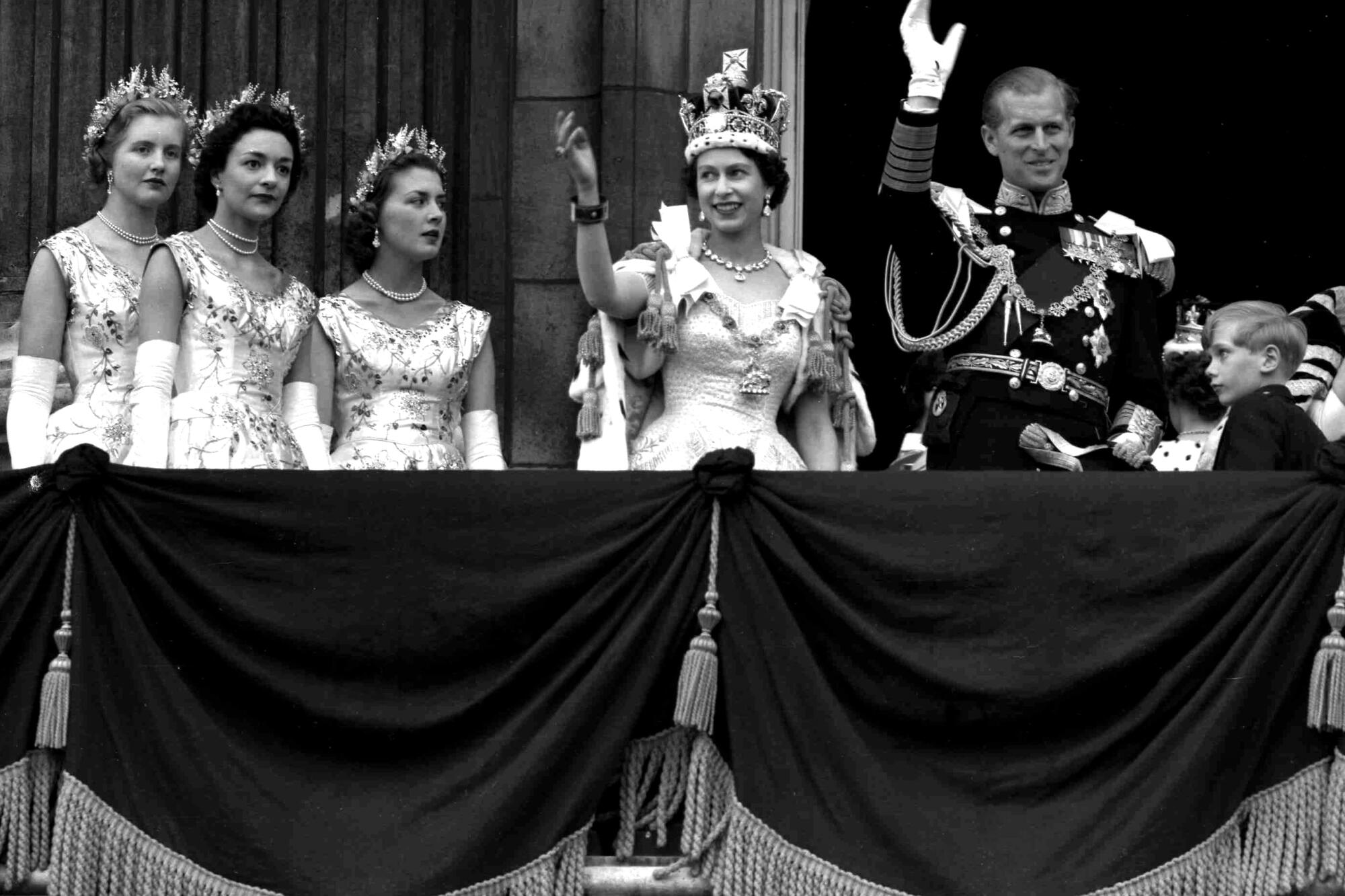 A woman wearing a dress and a crown is flanked by a man in white gloves and military uniform, right, and three women 