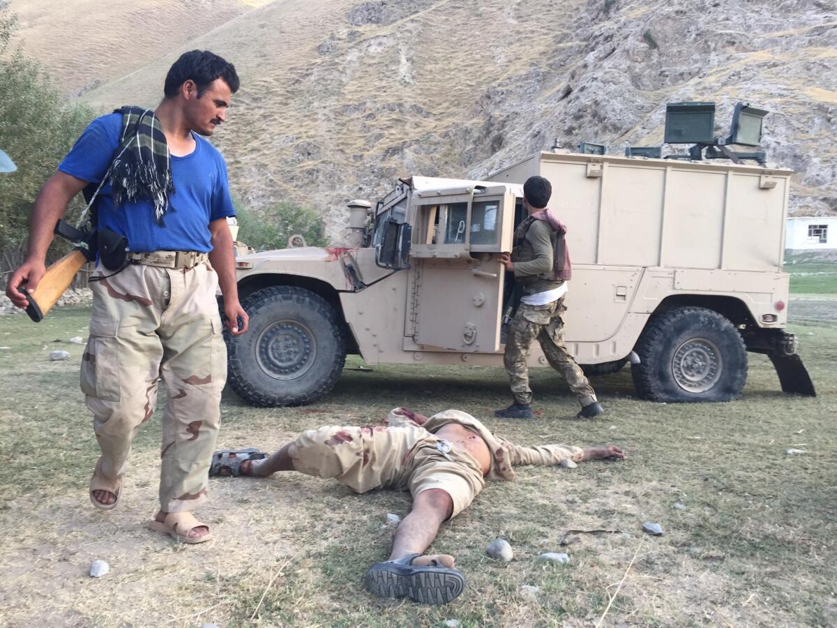 An Afghan policeman, left, stands over the body of a suspected Taliban leader killed in a July battle in Eshkamesh, Afghanistan.