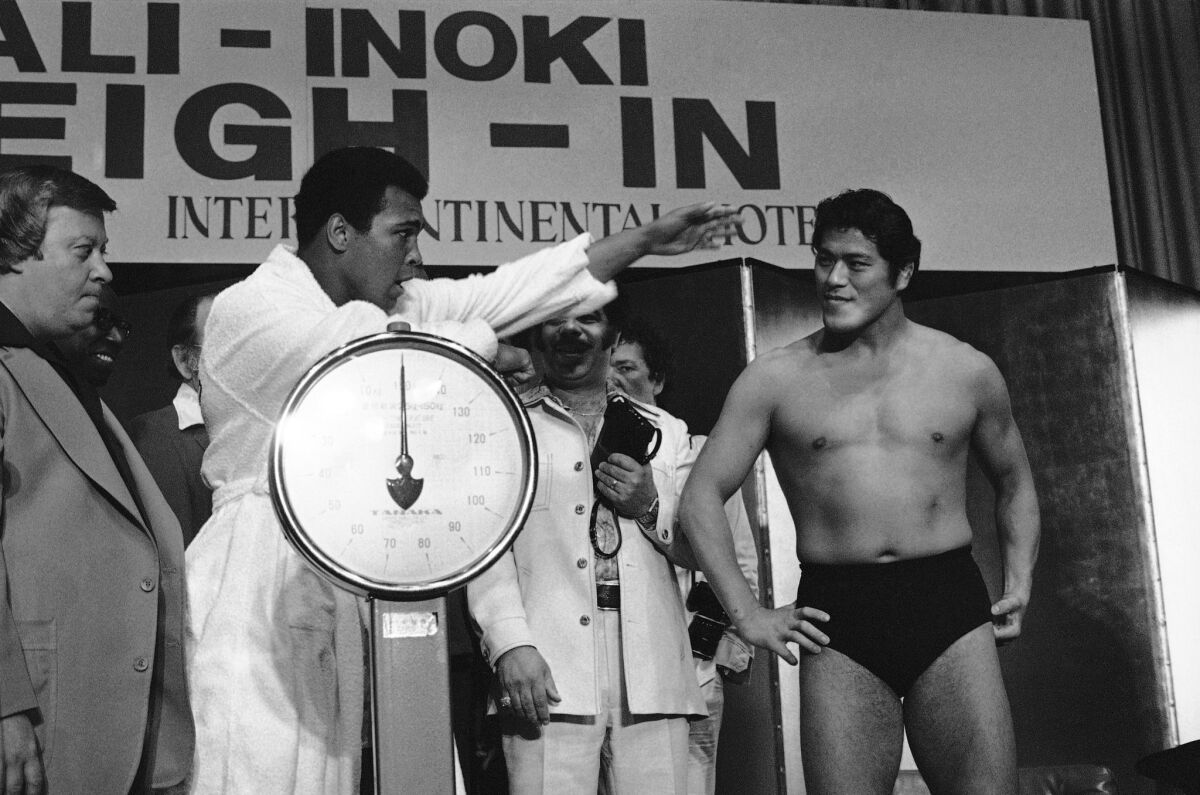 Muhammad Ali, standing on scale, gestures at his opponent, National Wrestling Federation world heavyweight champion Antonio Inoki. (Associated Press)