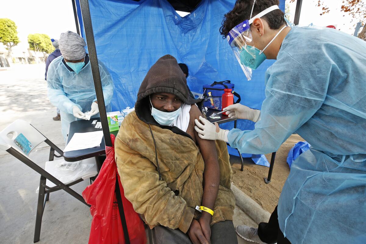 A person sitting in a chair has their left arm out of their jacket as a health worker gives them a shot in the arm