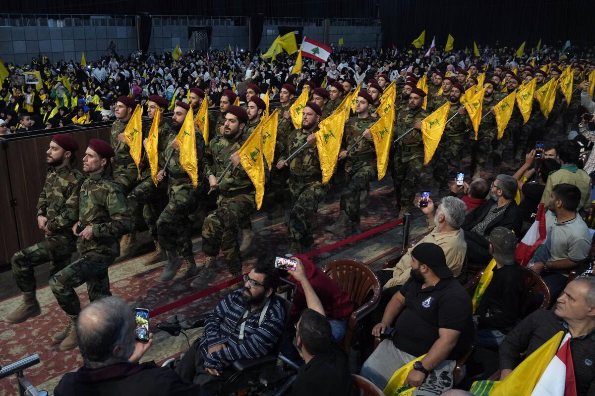 Fighters carrying guns and flags march along a carpeted aisle.