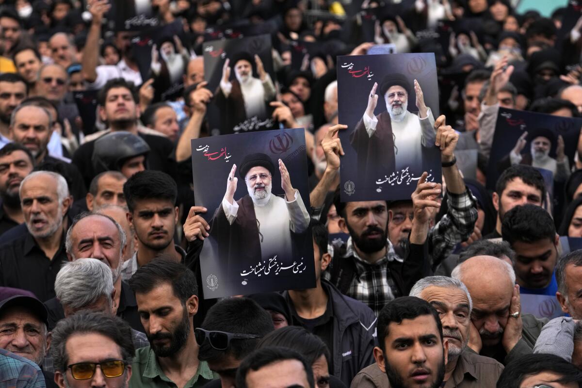 People in a crowd of mourners hold photos of President Ebrahim Raisi.