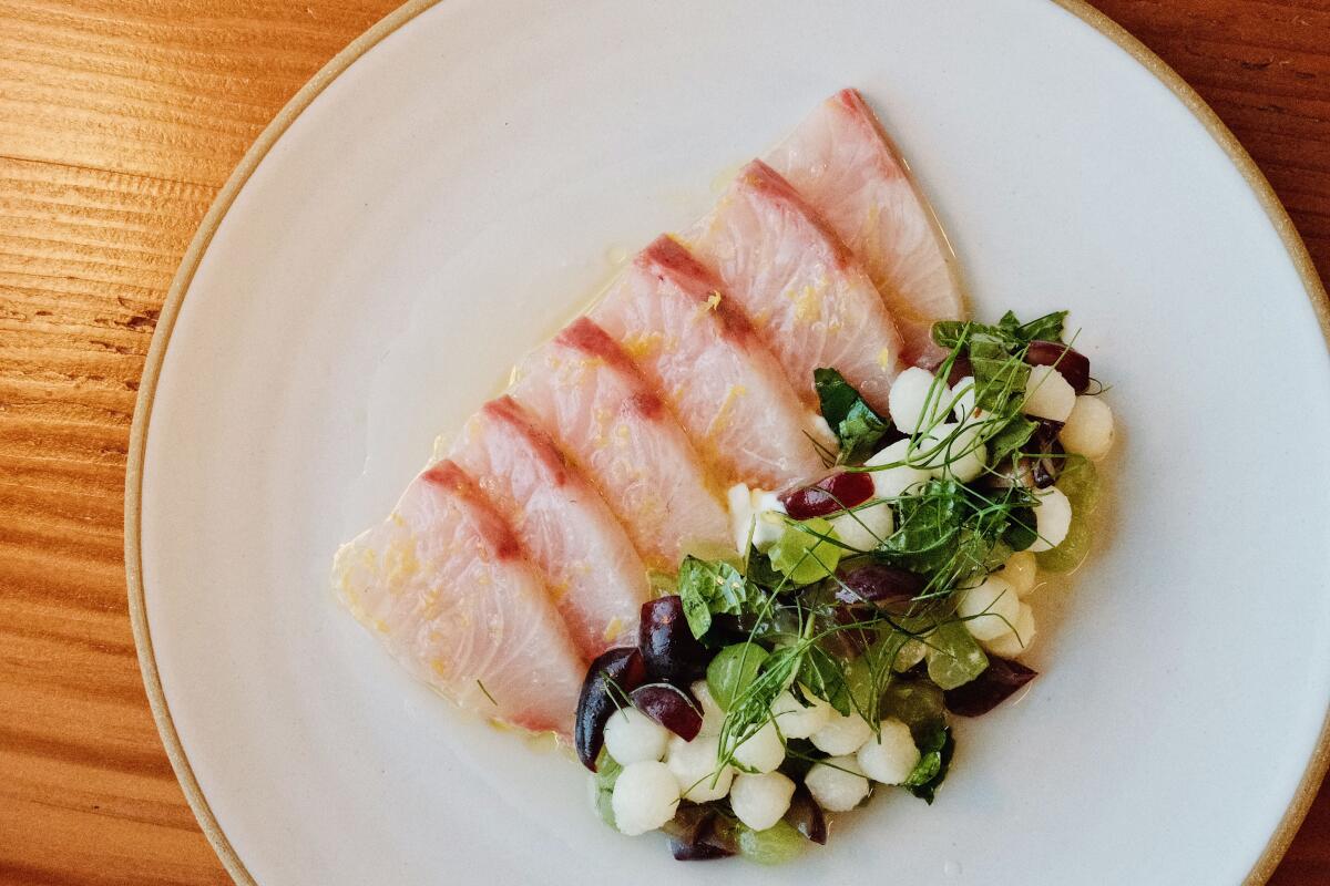 Slices of amberjack crudo next to an herb-topped salad of cucumber and grapes at Long Beach restaurant Olive & Rose