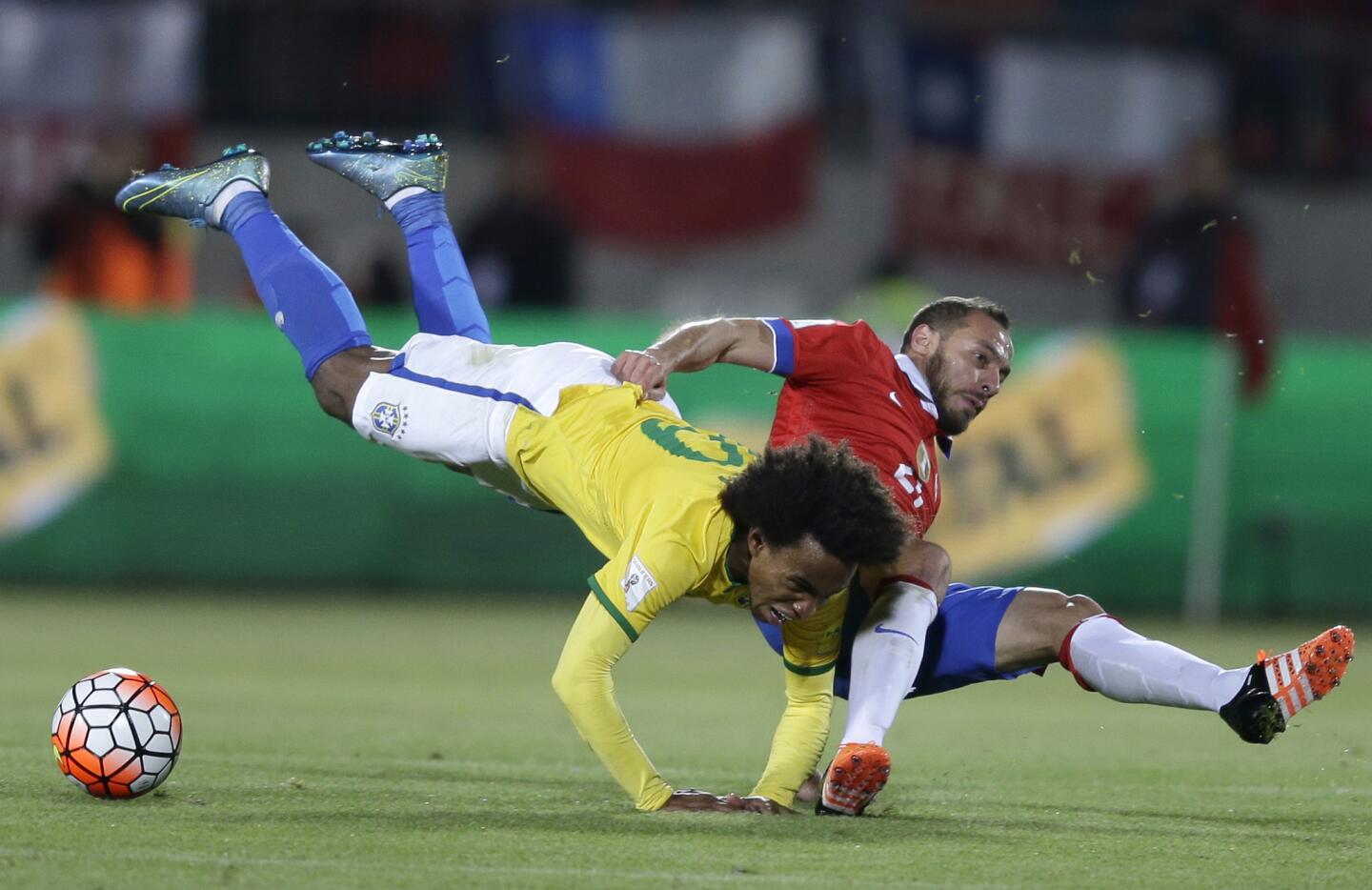 El brasileño Willian (i) es derribado por el chileno Marcelo Díaz en partido de la eliminatoria mundialista en Santiago, Chile.