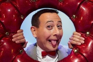 Paul Reubens sticking his tongue out and poking his head through a hole in an upholstered red donut.