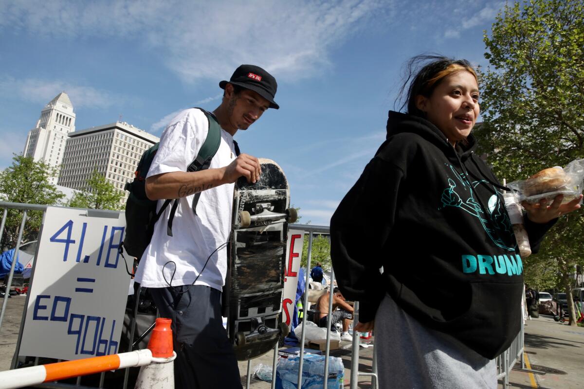 Two people walking, with barriers and L.A. City Hall behind them