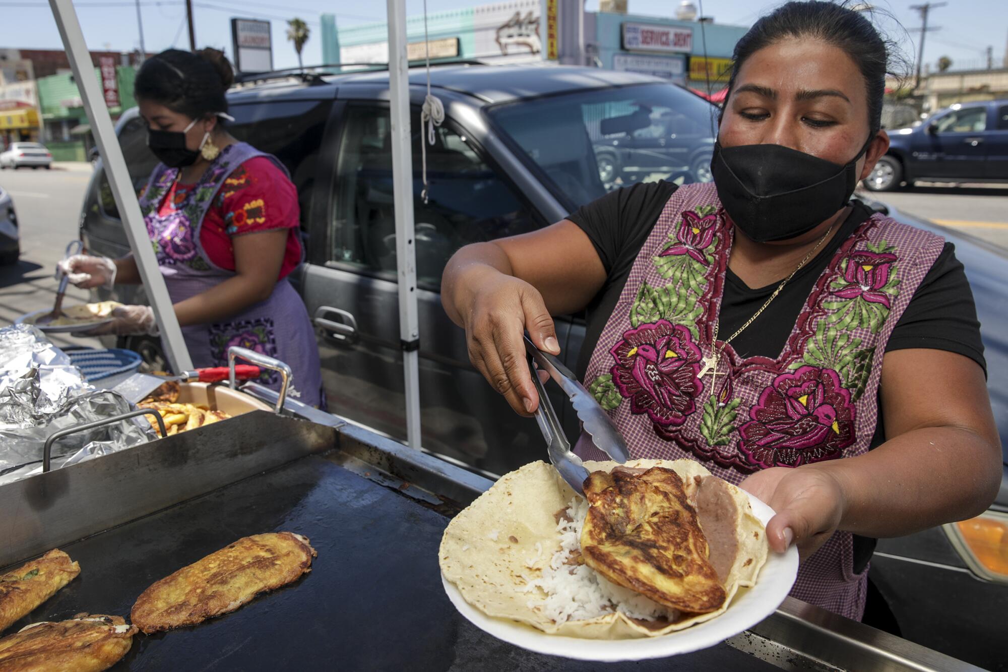 Two woman wearing masks cook outside