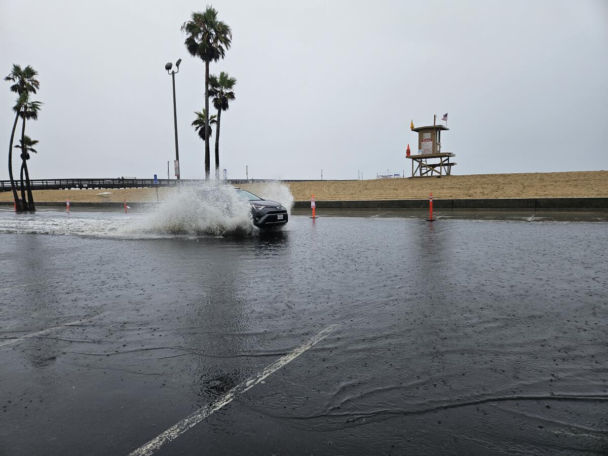 A car rushes through the water in the parking lot of the Balboa Pier. Part of the lot was flooded by early Sunday afternoon.