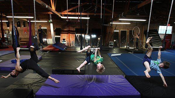 Instructor Sagiv Ben Binyamin, left, Benjamin Fernandez, 6, center, and Theo Fernandez, 9, balance on the trapeze at Cirque School in Hollywood. At Cirque School you can learn how to be an acrobat, from aerial tricks to tumbling to fabric performance to trapeze.