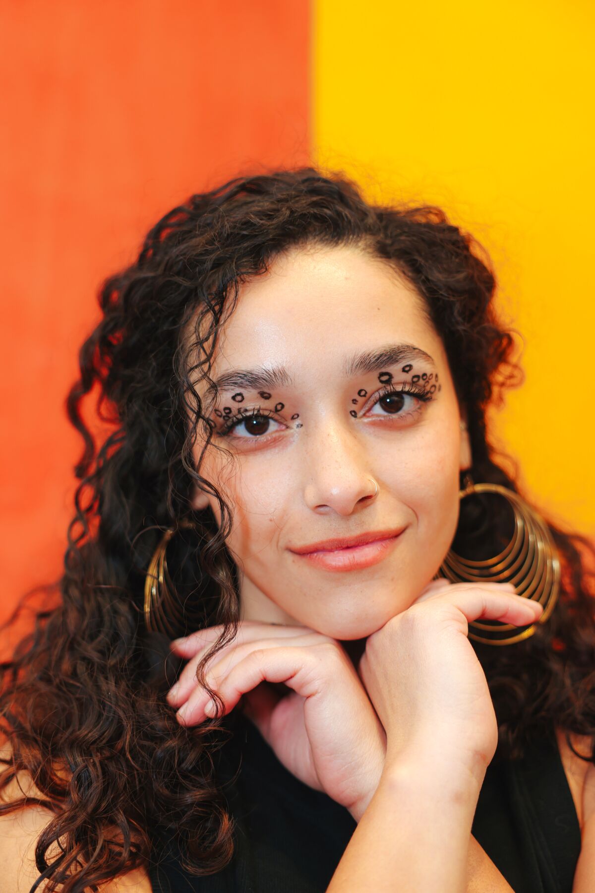 A woman stands in front of a painting that incorporates bands of orange and yellow.