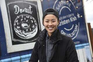 "Top Chef" winner Kristen Kish poses in front a food truck wearing a backwards cap and a layered jacket