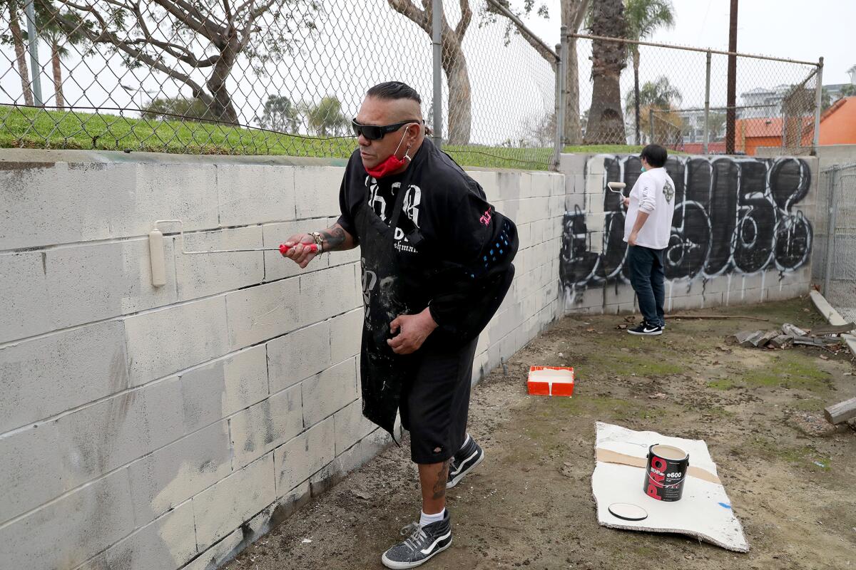 Huntington Beach native Adam "Bushman" Orozco, 59, left, and his son Thunder, 22, right, clean up graffiti on a wall.  