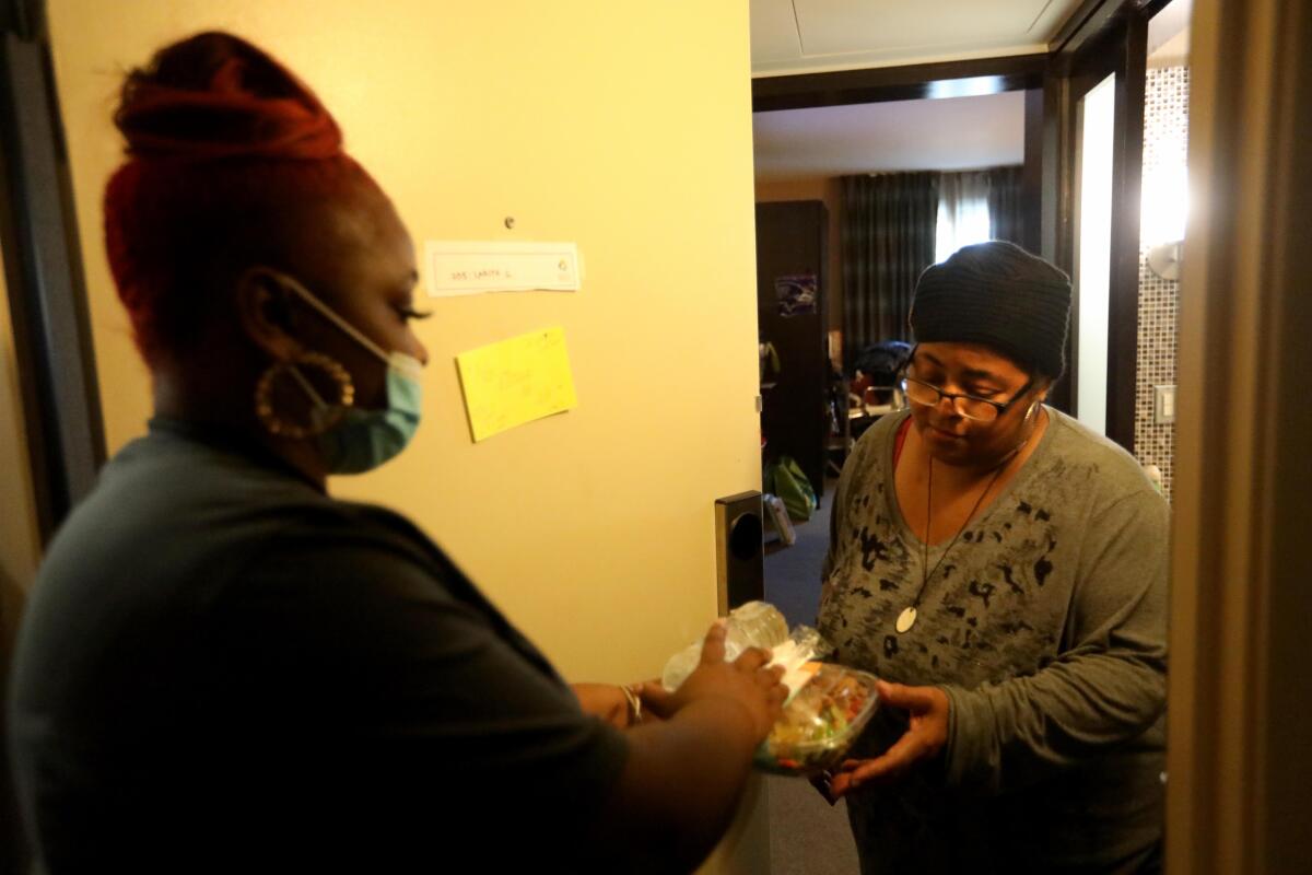 Mia Rogers, 23, left, gives Project Roomkey guest Larita Garner, 61, her lunch at a Project Roomkey hotel in Los Angeles.