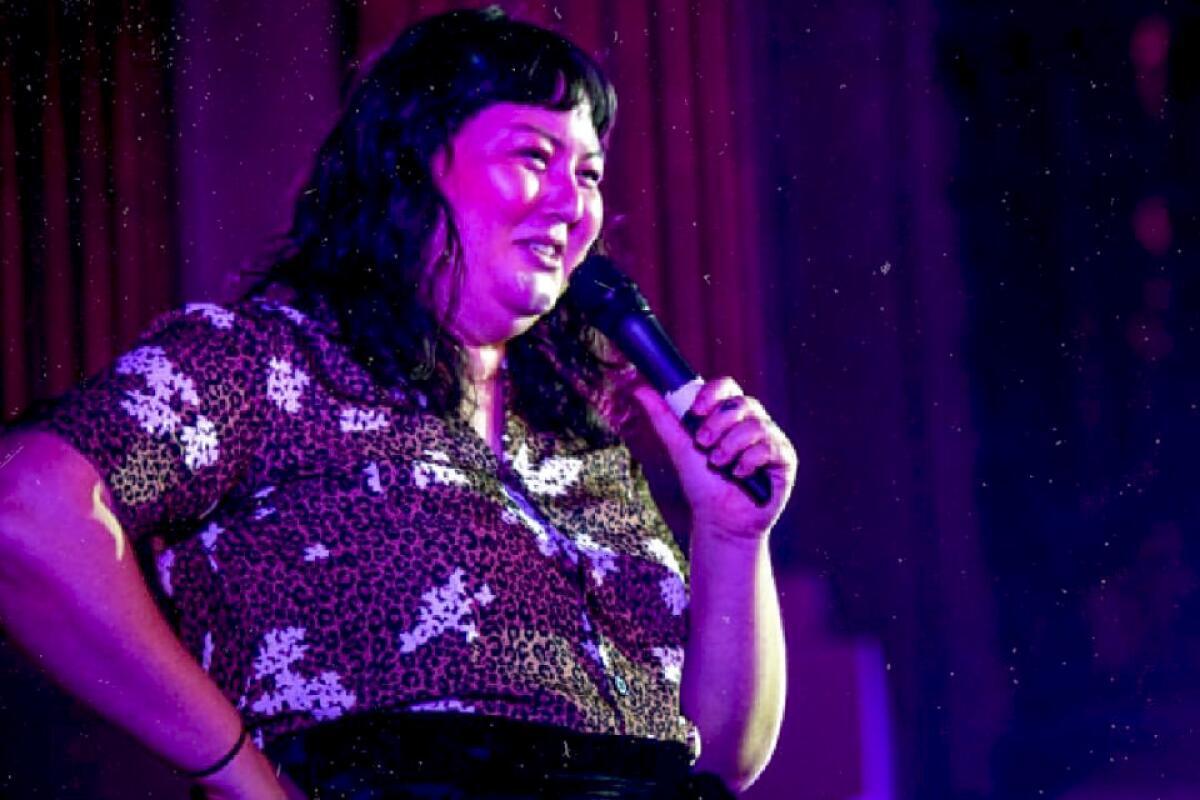 A woman tells a joke onstage at a comedy club.