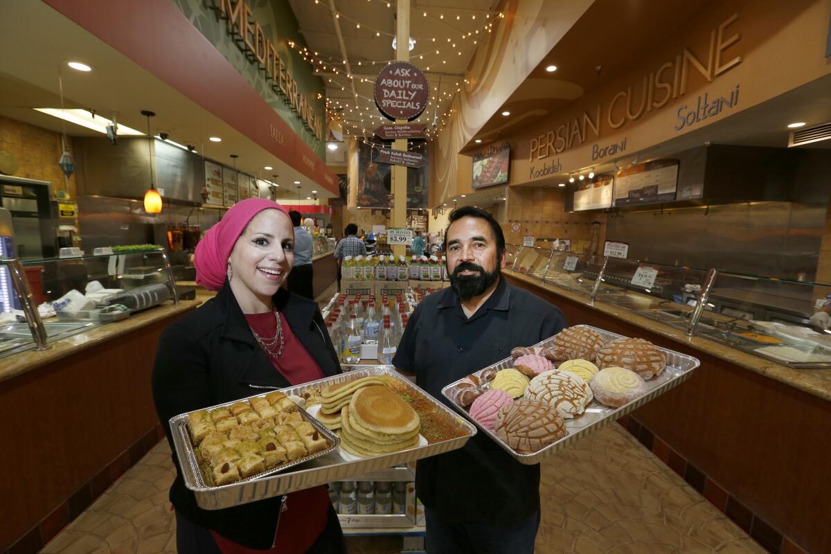 Rida Hamida, left, a Muslim of Palestinian descent who holds tours in Anaheim's Little Arabia, holds Arab deserts, while Benjamin Vazquez shows off Latino desserts at Fresh Choice Marketplace in Anaheim.