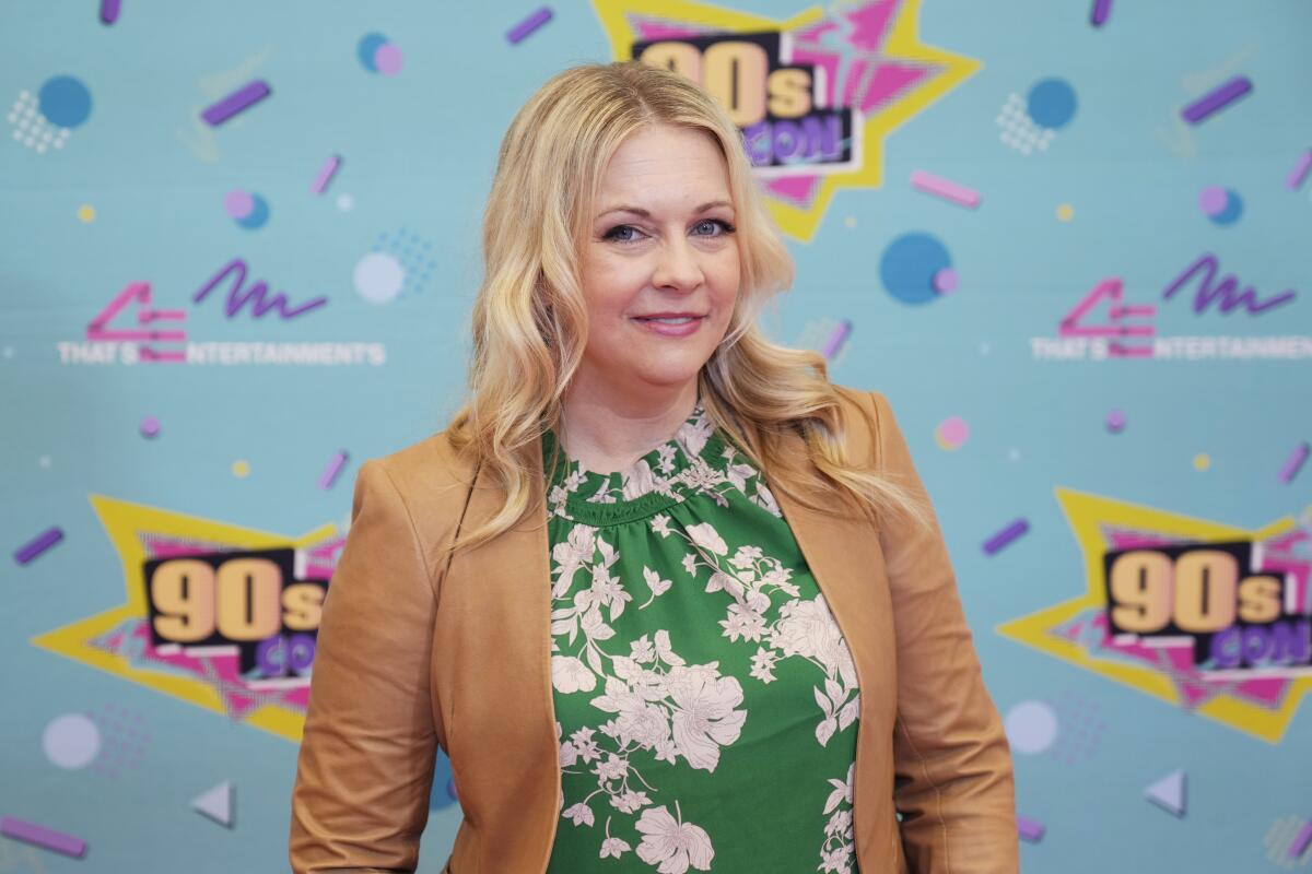 Melissa Joan Hart smiles in front of a colorful backdrop labeled '90s Con.