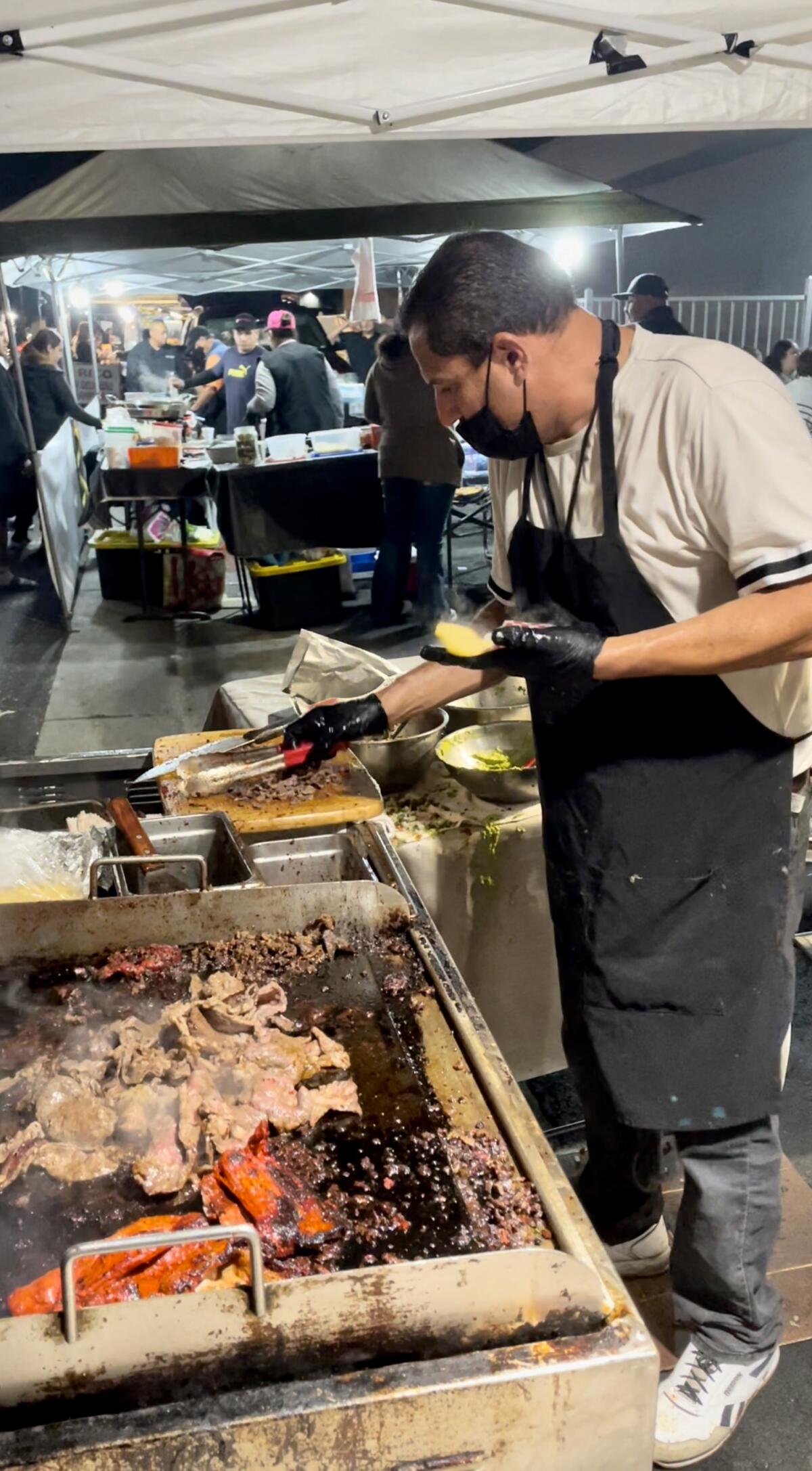 A taquero grills meat for tacos for Cachanilla at the Santa Ana de Noche market.