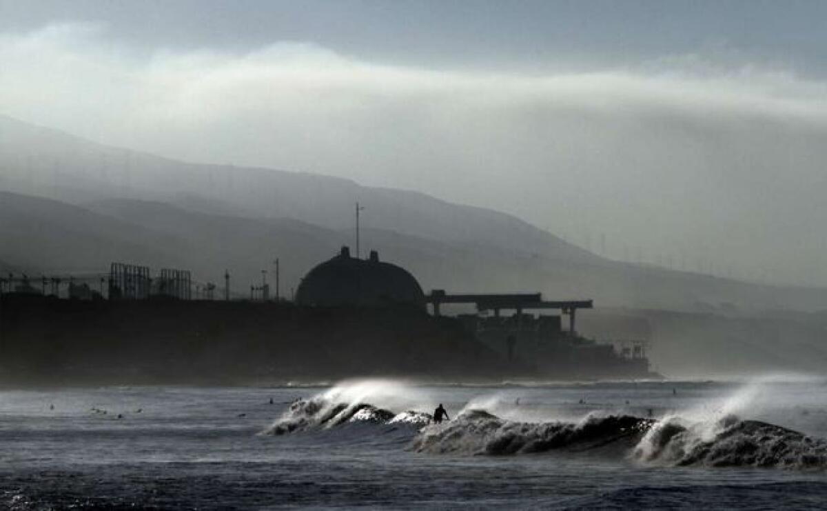 Surfers ride the waves at Lower Trestles near San Clemente as the darkened San Onofre nuclear plant looms in the distance.