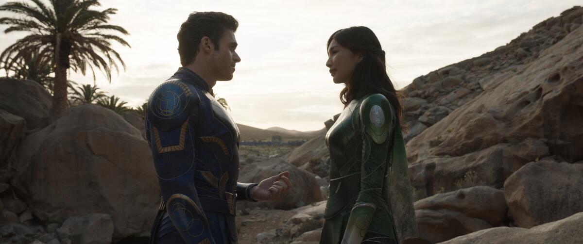 A man in a blue superhero suit facing a woman in a green superhero suit