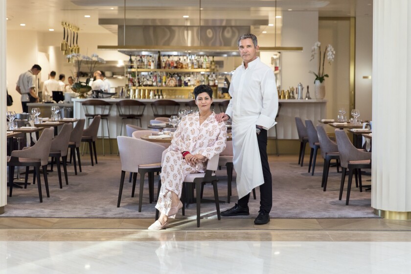 A woman sitting and a man standing in front of their restaurant.