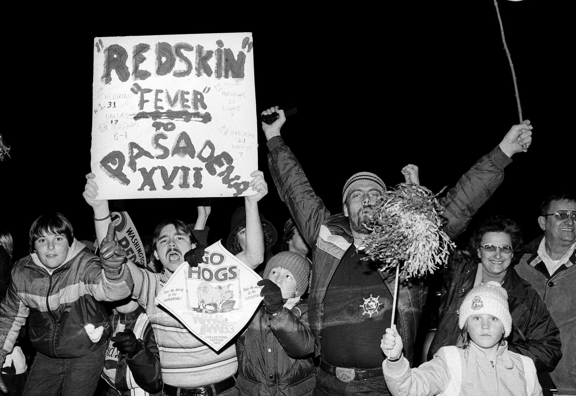 Washington fans wave signs as members of the team leave Redskins Park