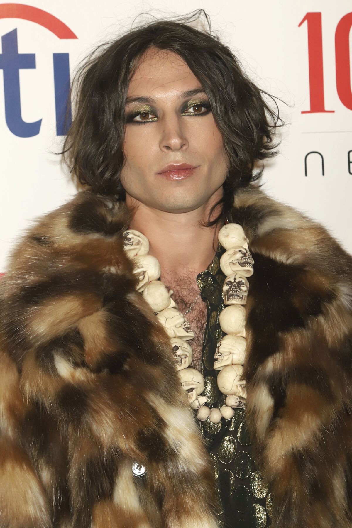 A person with sparkling eye makeup and dark hair wearing a fur coat.
