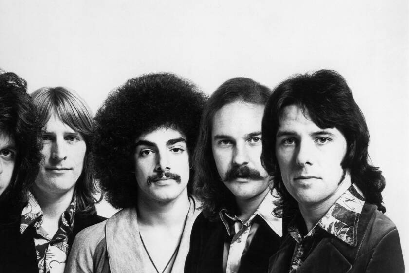 A black and white photo of Journey's founding members in '70s style attire and hairdos looking forward