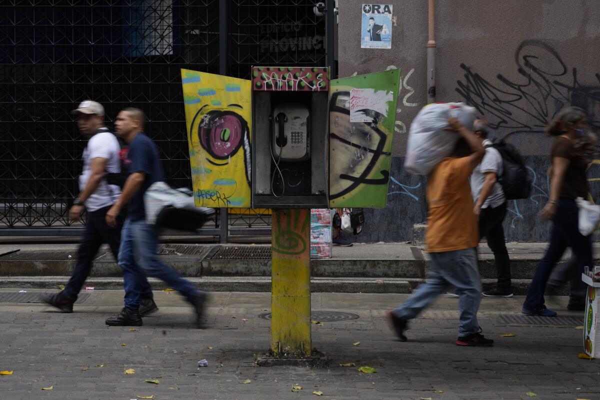 Pedestrians walk past an out of service phone booth.