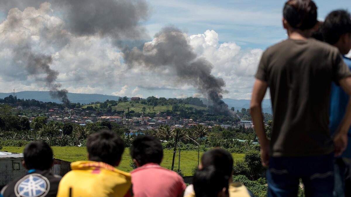 People watch as smoke billows from houses after aerial bombings by Philippine Airforce planes on Islamist militant positions in Marawi.