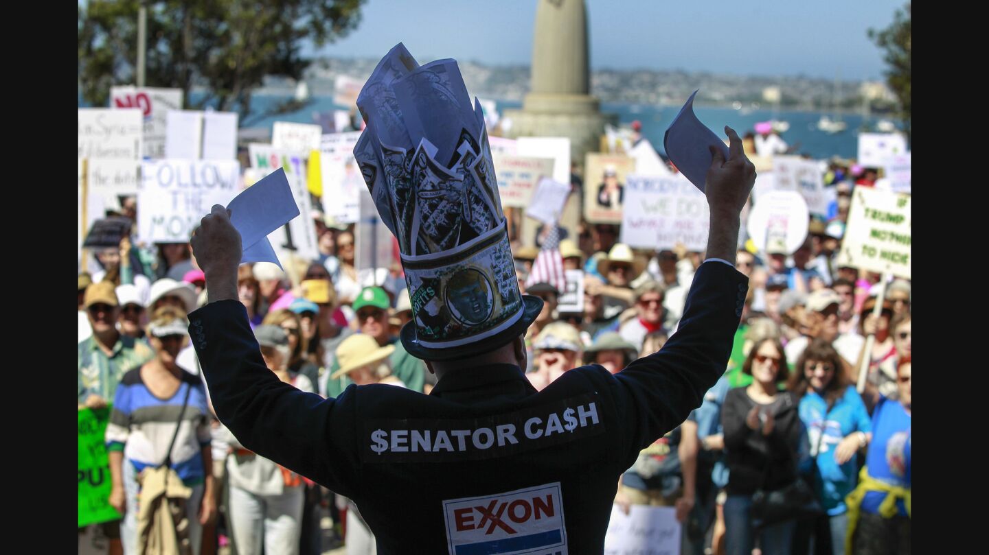 Michael Mufson, who is in character as Senator Cash, waves paper that represents money as he speaks to the crowd gathered at the San Diego County Administration Center.