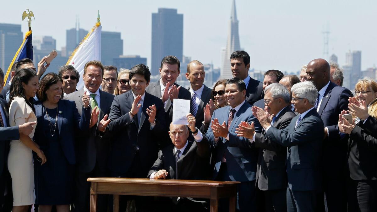 California Gov. Jerry Brown holds up climate legislation at a signing ceremony on Treasure Island on Tuesday while former Gov. Arnold Schwarzenegger, third from left, looks on.
