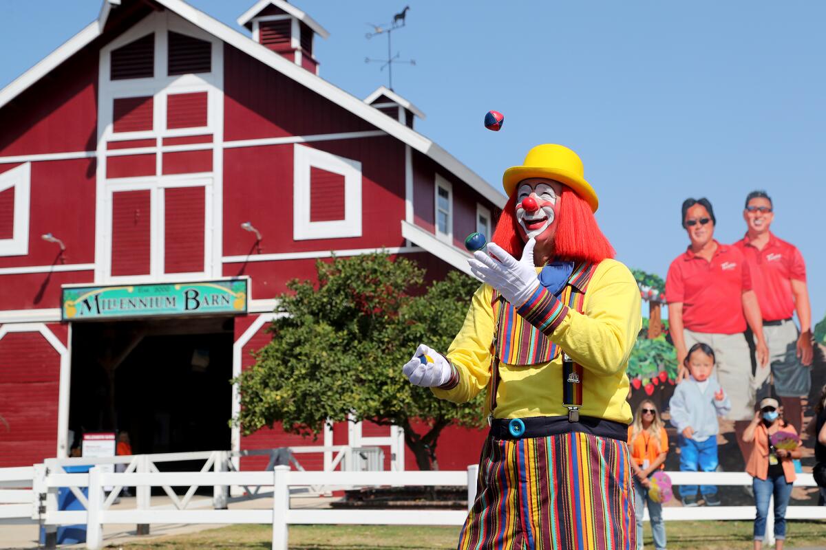 A clown juggles in front of a barn