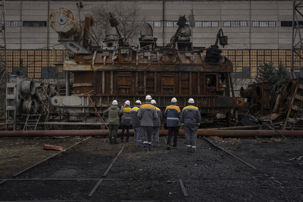 Varios trabajadores de una central eléctrica miran un enorme transformador de voltaje dañado 