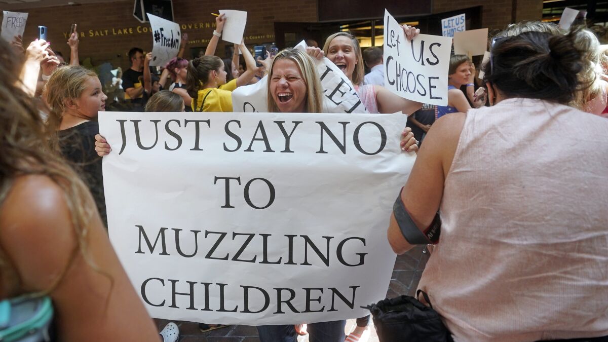 A woman smiles and shouts while holding a poster that says, "Just say no to muzzling children."