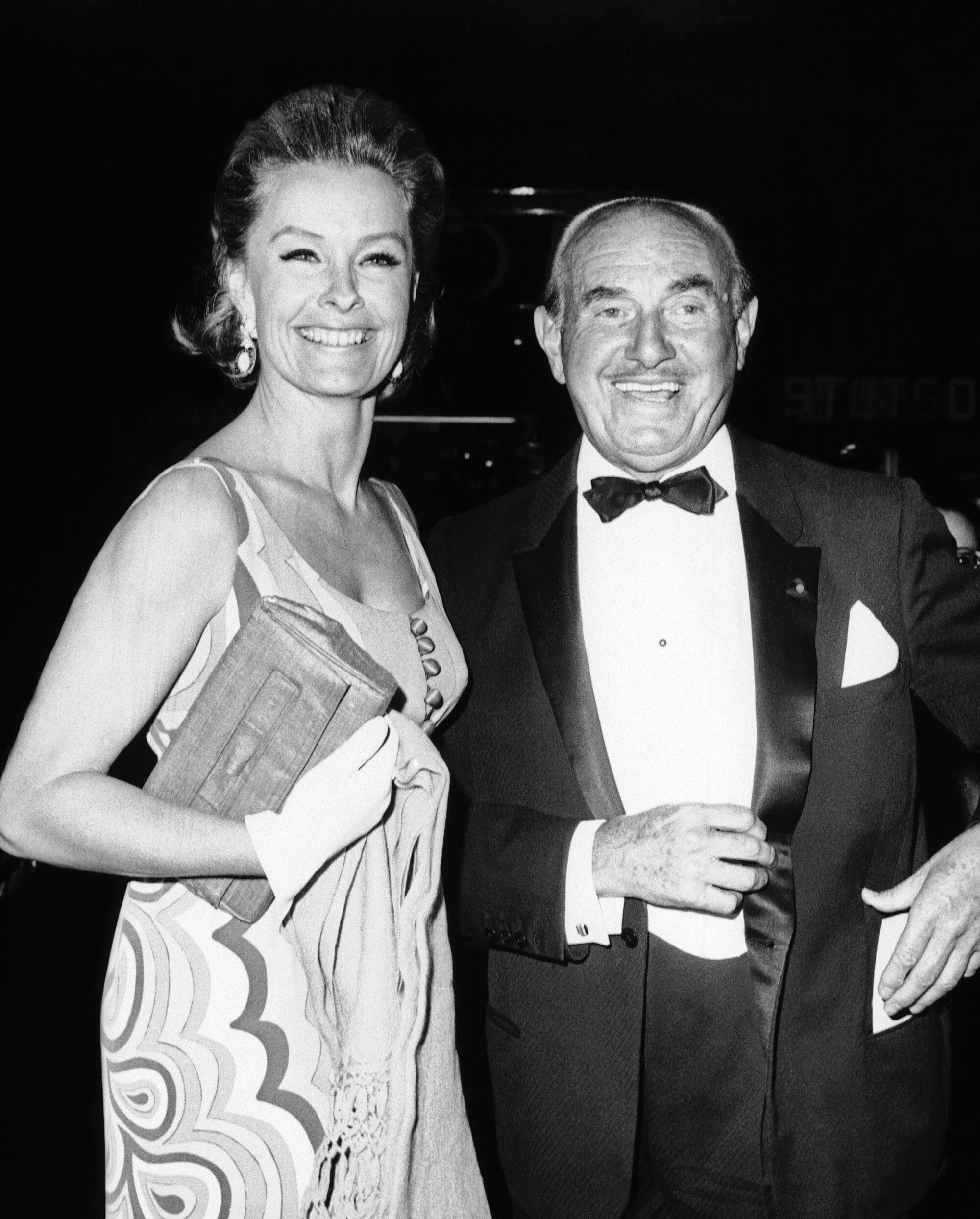 Warner Bros. mogul Jack L. Warner and Dina Merrill smile while dressed in evening wear in 1966.