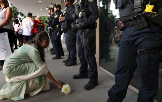 A woman leaves a flower at the feet of federal officers standing guard at the Federal Building.