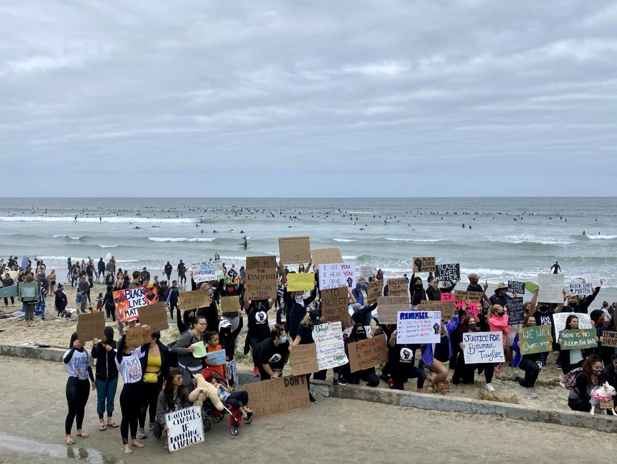 Protesters gather with signs during the Paddle for Peace at Tourmaline as surfers go in the ocean to honor George Floyd.