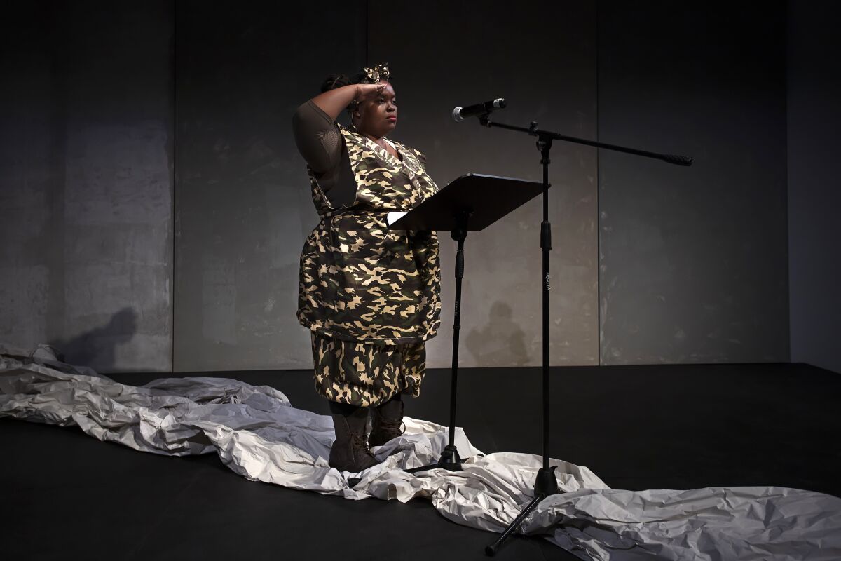 A woman in an African print dress stands at a microphone.