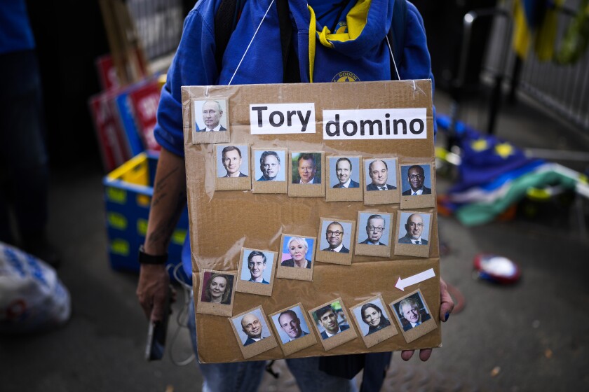 A protester holds a placard with photographs of British Prime Minister Boris Johnson, bottom right, his government cabinet members and Russia President Vladimir Putin, top left, outside the Houses of Parliament, in London, Wednesday, July 6, 2022. A defiant British Prime Minister Boris Johnson is battling to stay in power after his government was rocked by the resignation of two top ministers. His first challenge is getting through Wednesday, where he faces tough questions at the weekly Prime Minister's Questions session in Parliament, and a long-scheduled grilling by a committee of senior lawmakers. (AP Photo/Matt Dunham)