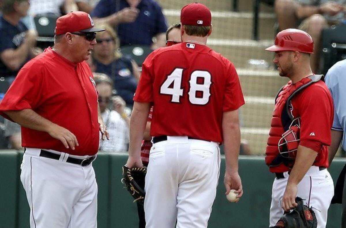 Angels Manager Mike Scioscia, left, talks to a trainer after starting pitcher Tommy Hanson (49) felt tightness in his triceps while warming up for the fourth inning Wednesday.