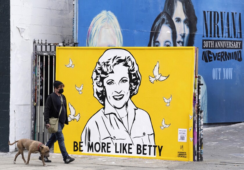 A man walks a dog past a new mural of the late actress Betty White by artist Corie Mattie, Tuesday, Jan. 13, 2022, in Los Angeles. Mattie added a QR code to the mural so people walking by can donate to the local shelter Wagmor Pets Dog Rescue in honor of White, an animal welfare advocate. White died Dec. 31, 2021, at age 99. (AP Photo/Chris Pizzello)