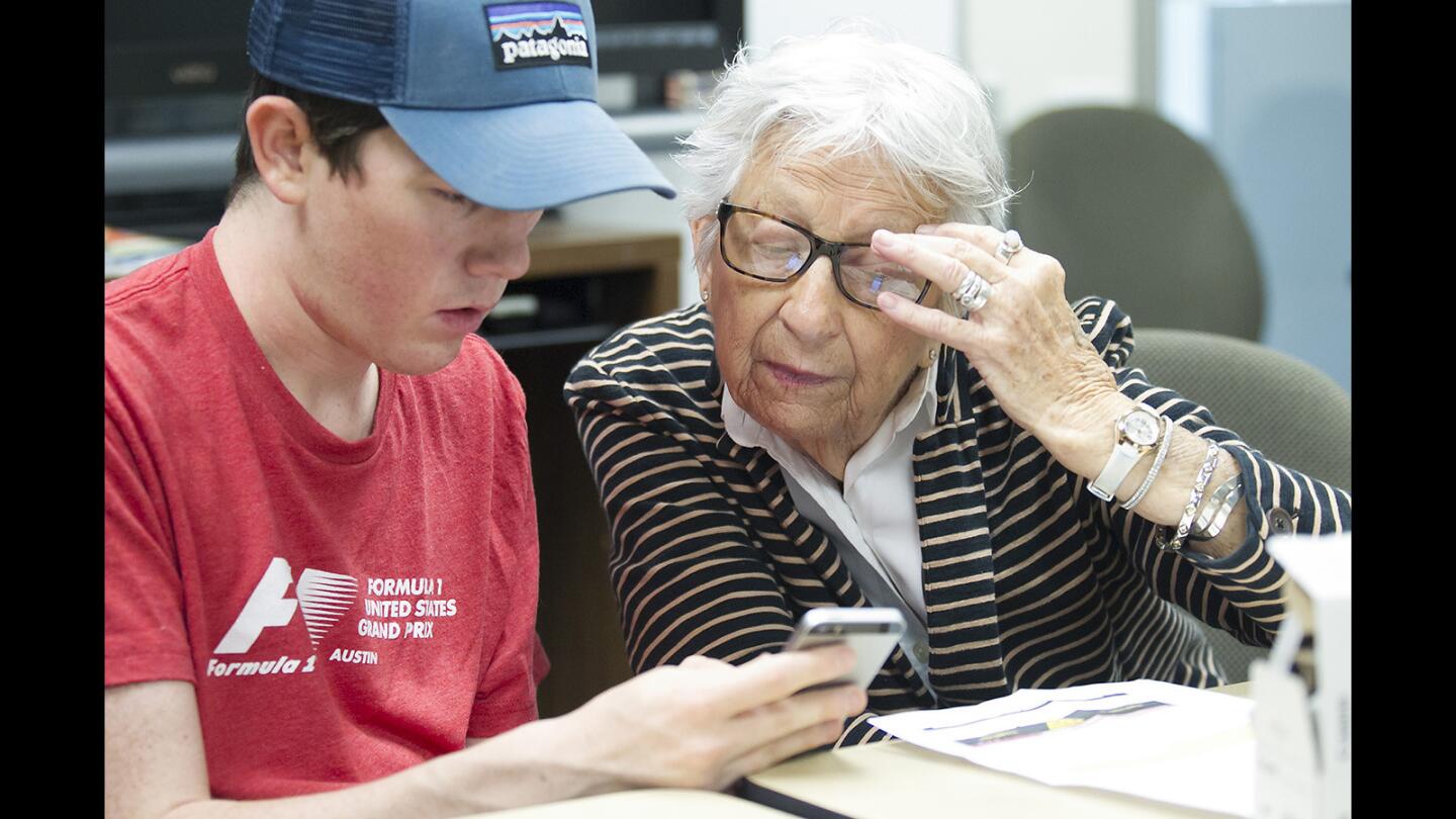 Sage Hill student Michael Justice, left, helps Skipper Lynn with a smartphone app that arranges for a cab during the Cyber-Senior Workshop at the Susi Q Senior Center on Wednesday. The program helps seniors navigate modern technology, especially on their smartphones.