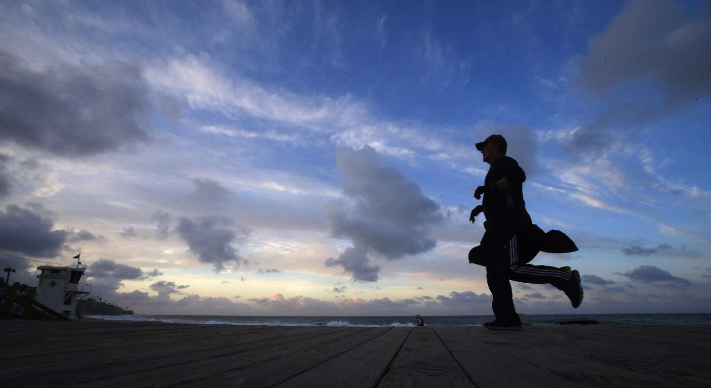 Rain clouds start to clear as a jogger gets in an early morning run on the boardwalk in Laguna Beach.